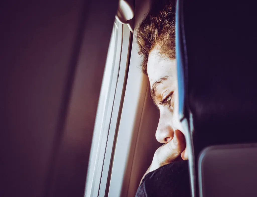 Ein junger Mann blickt mit ängstlichem Gesichtsausdruck aus dem Flugzeugfenster – Symbol für Aviophobie und die Suche nach Tabletten bei Flugangst.