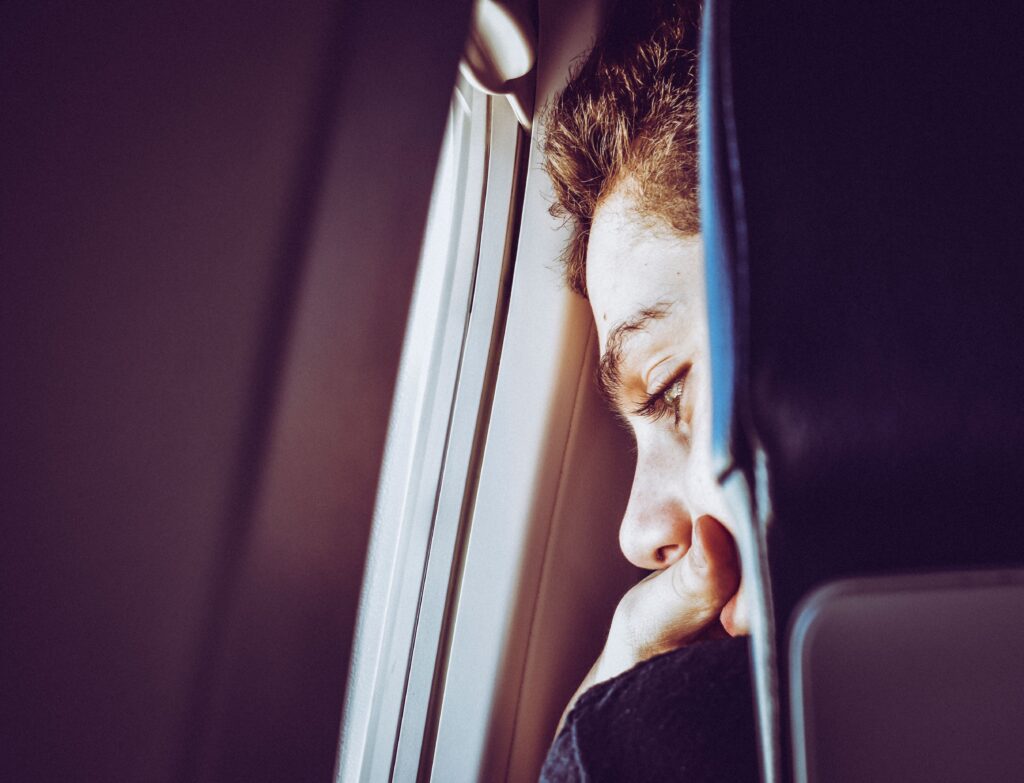 Ein junger Mann blickt mit ängstlichem Gesichtsausdruck aus dem Flugzeugfenster – Symbol für Aviophobie und die Suche nach Tabletten bei Flugangst.