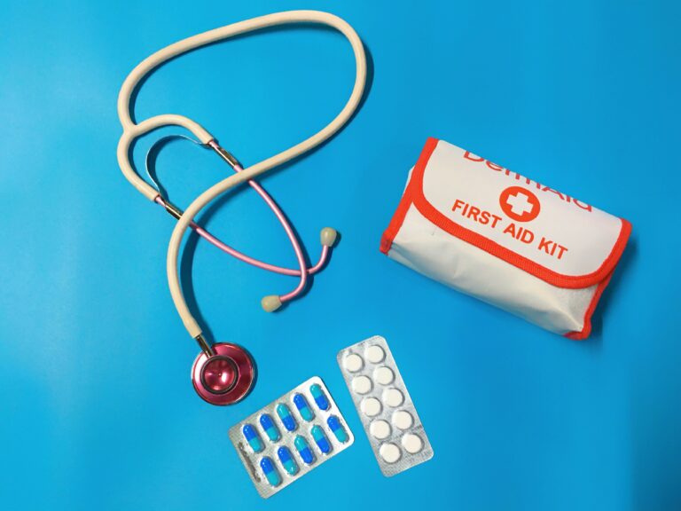 Ein Erste-Hilfe-Set, ein Stethoskop und Medikamente auf blauem Grund als symbolische Basis für eine gut sortierte Reiseapotheke für Kinder.