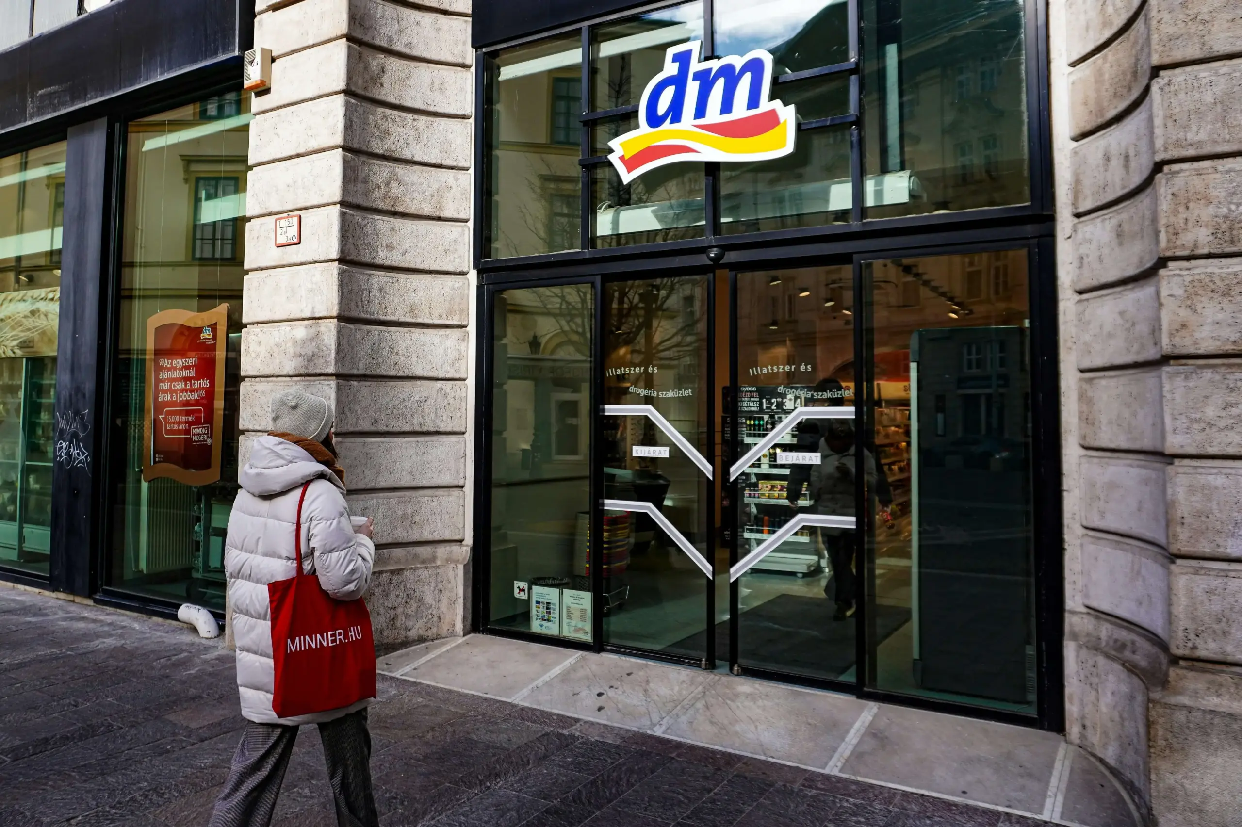 Außenansicht eines dm Drogeriemarktes mit einer Passantin, ideal für den Kauf von Produkten für das Reiseapotheke Set dm wie Mückenschutz und Erste-Hilfe-Sachen.