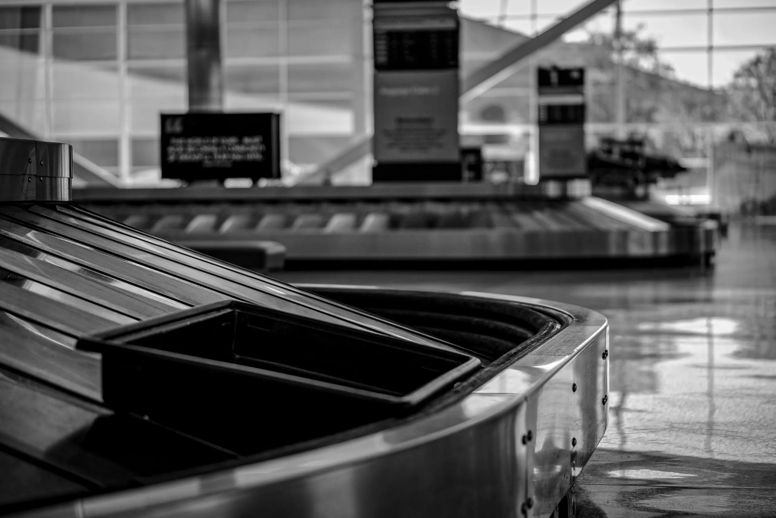 Ein leeres Gepäckband am Flughafen in Schwarz-Weiß als Symbol dafür, wie man mit den richtigen Handgepäck Maßen von Ryanair, Lufthansa und Easyjet Zeit spart.