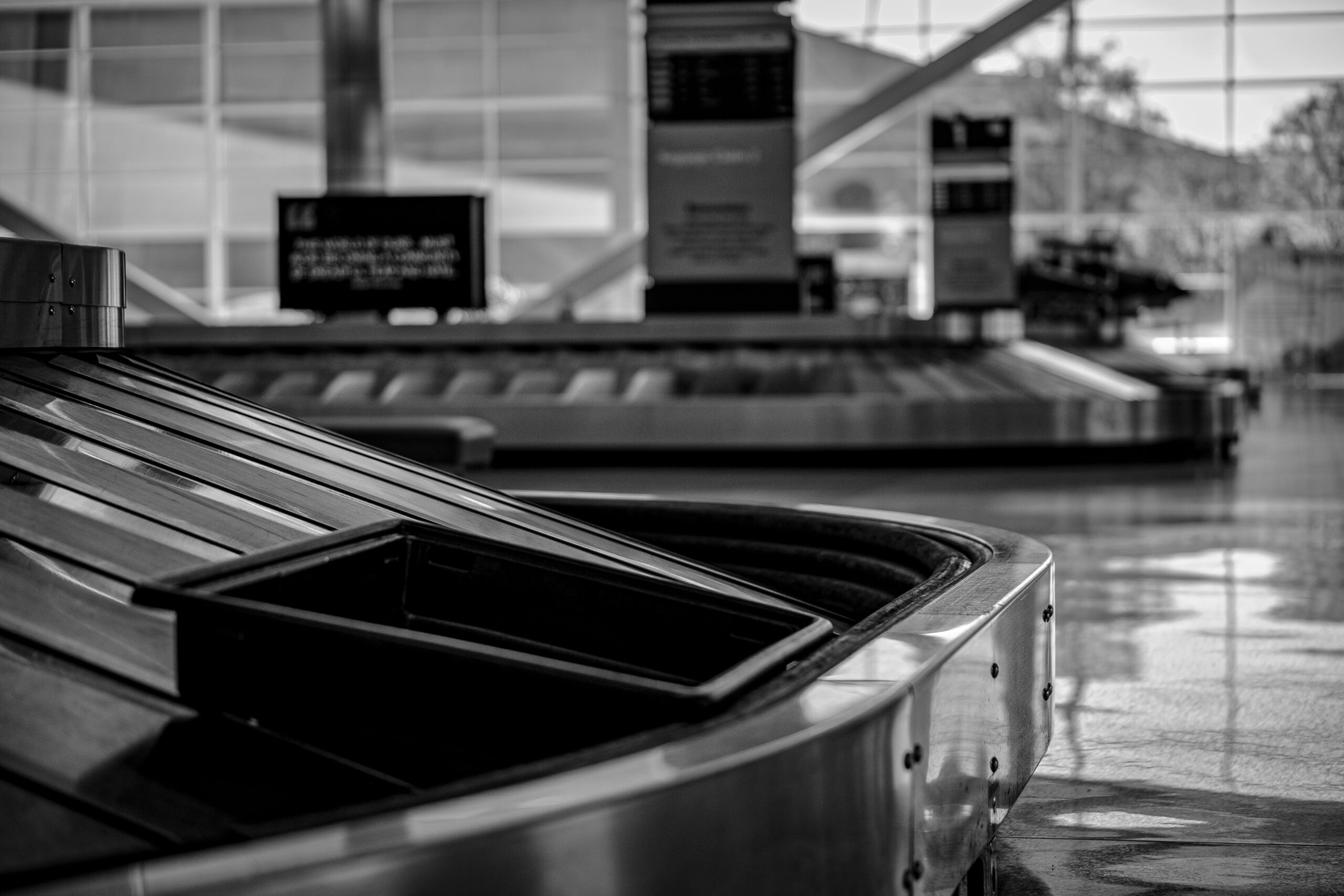 Ein leeres Gepäckband am Flughafen in Schwarz-Weiß als Symbol dafür, wie man mit den richtigen Handgepäck Maßen von Ryanair, Lufthansa und Easyjet Zeit spart.